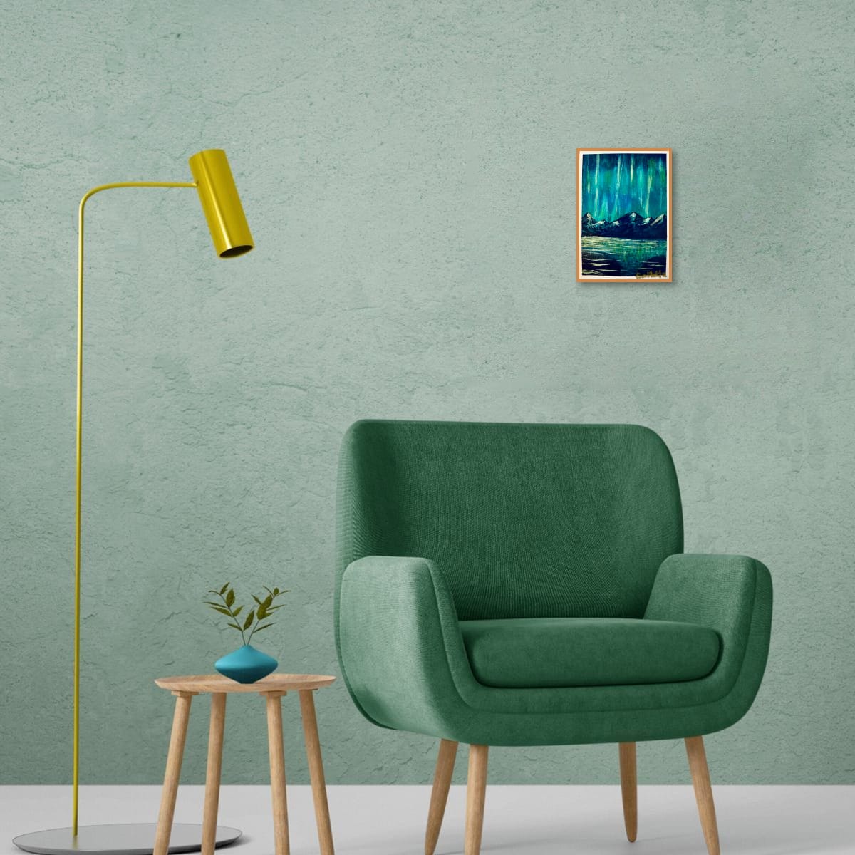 Modern green armchair with a yellow floor lamp and a small table against a light green wall with an A6 original acrylic mini painting of teal aurora lights over snow-capped mountains with reflections on water by artist Eman Khalifa