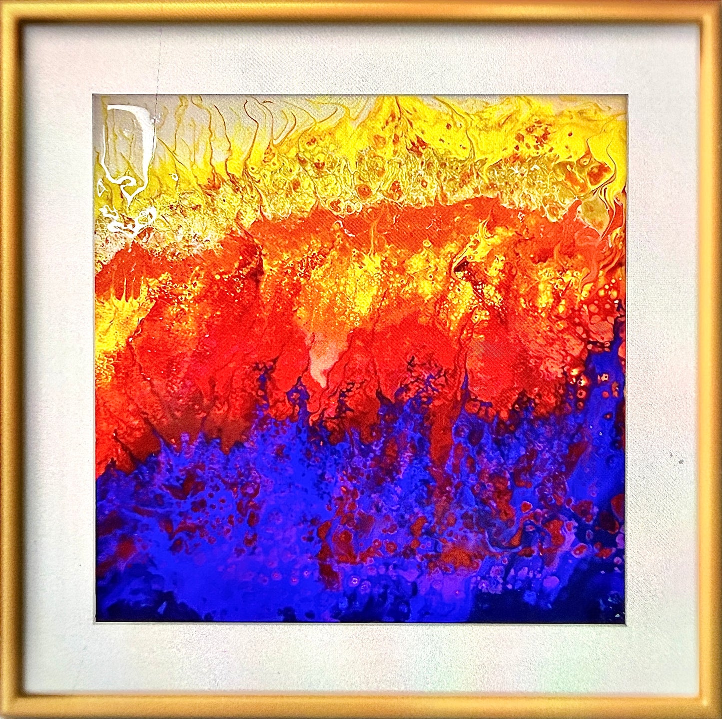 A framed abstract painting featuring a bold horizontal color gradient with bright yellow at the top, transitioning through vivid red in the middle, to deep blue at the bottom, enclosed in a gold frame with a white mat.