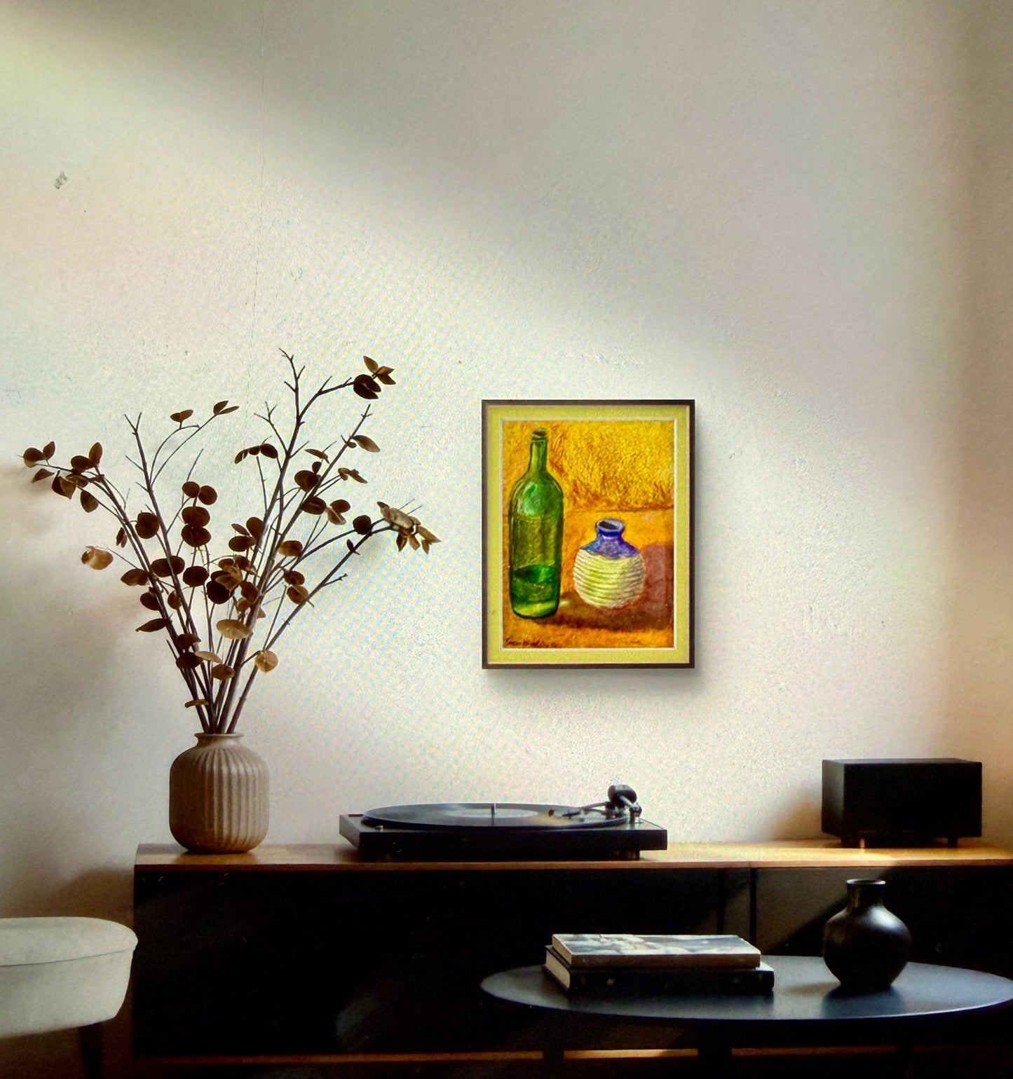 Room interior with a table, vase with branches, record player, and framed artwork on the wall.