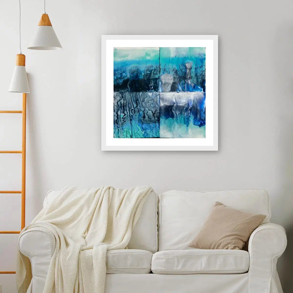 Framed abstract art piece on a wall above a white sofa with a blanket and pillow.