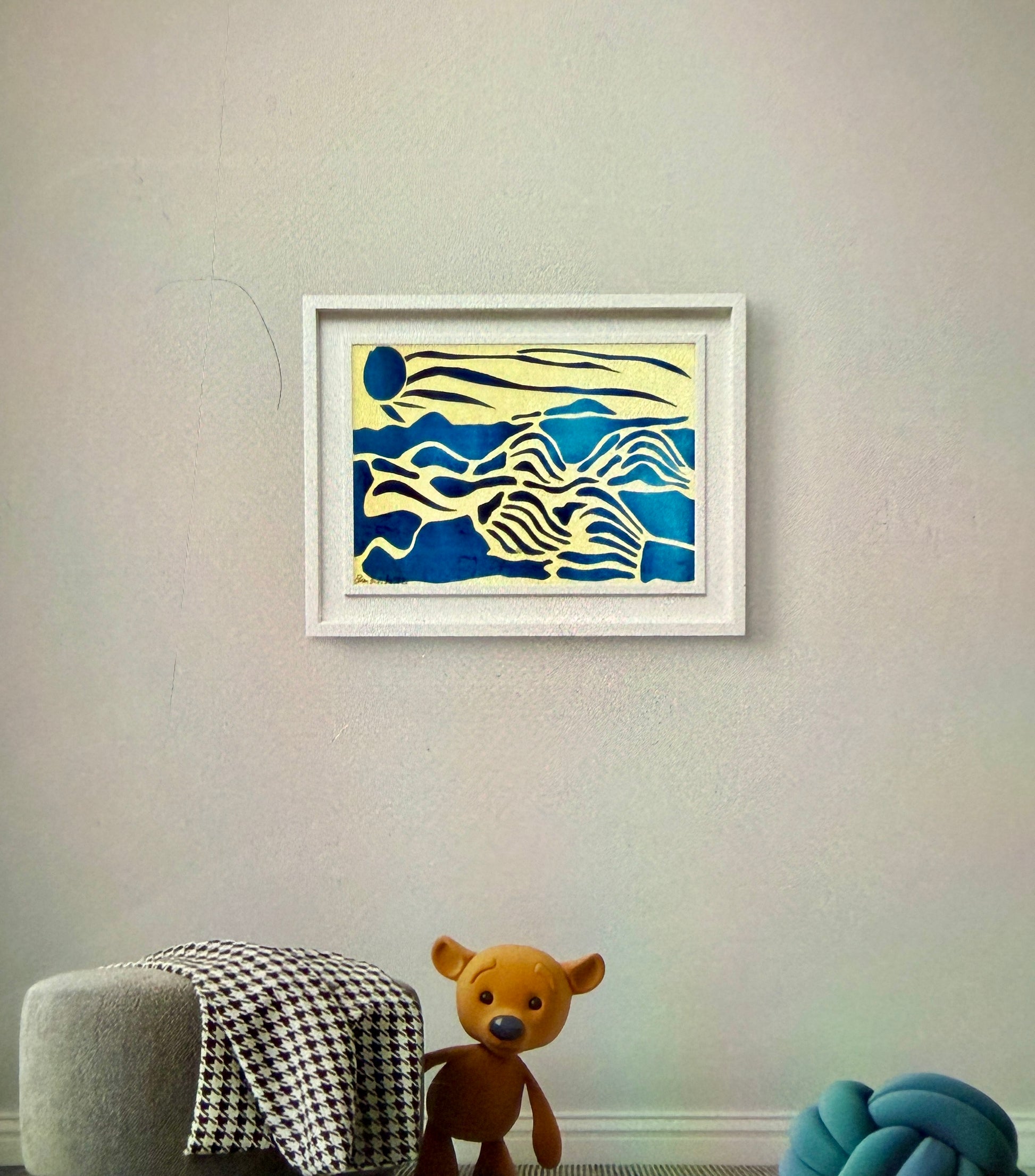 Framed abstract artwork on a wall with a teddy bear and stool below.