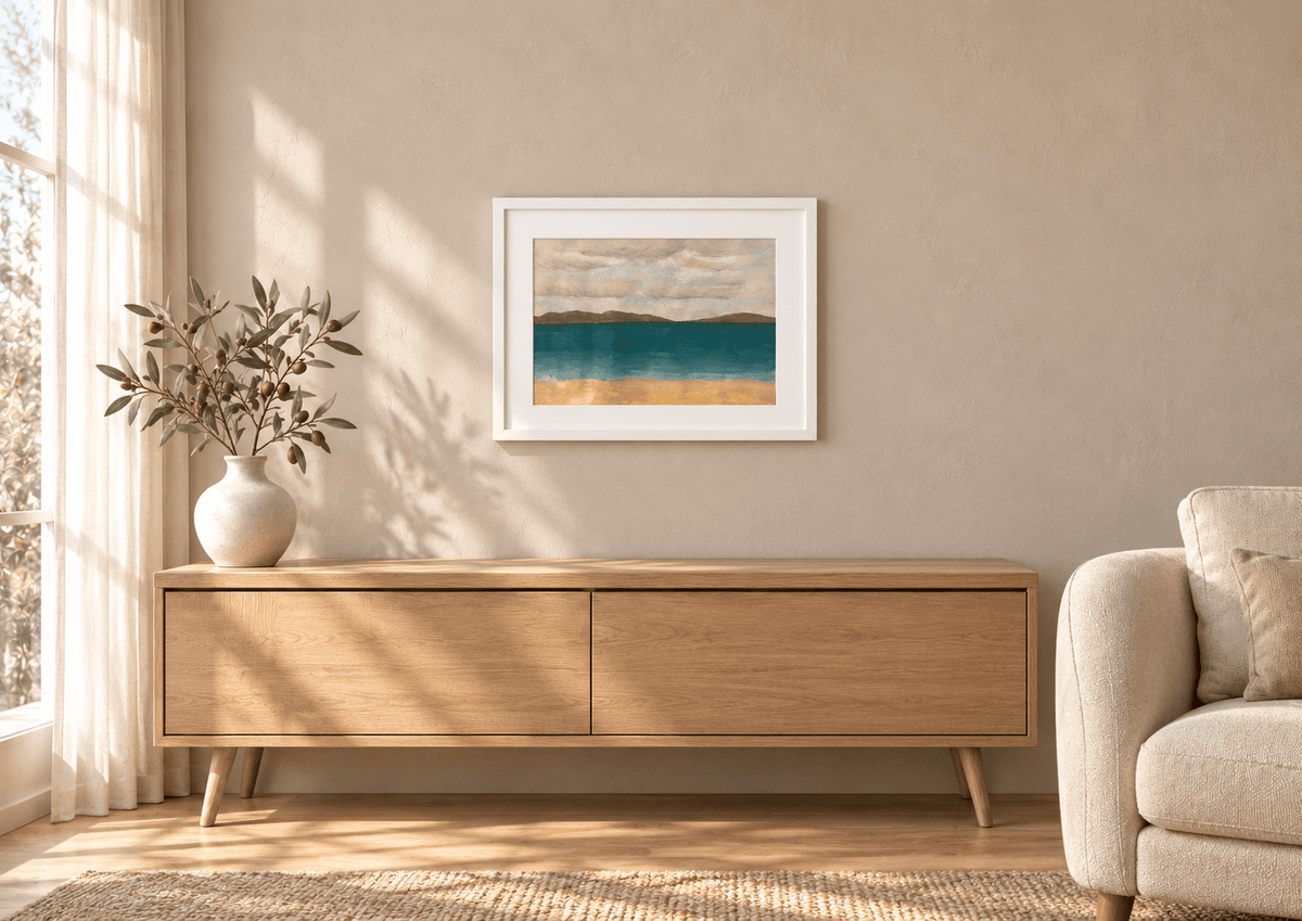 Solace by Eman Khalifa, a tranquil teal sea beneath a soft grey sky, with distant brown land and a warm sandy foreground framed above an oak console