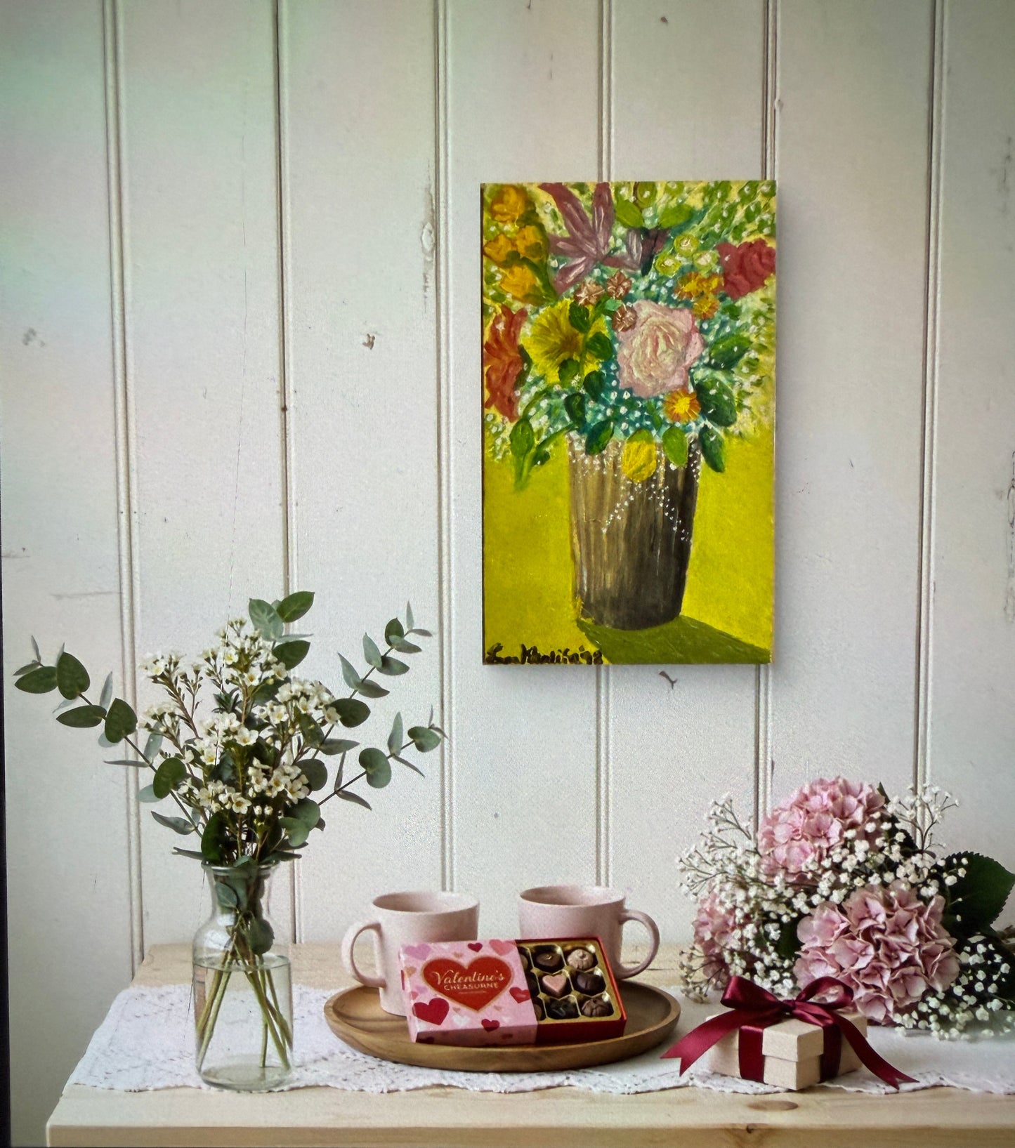 Decorative setup with a painting, flowers, and a teacup on a white surface.