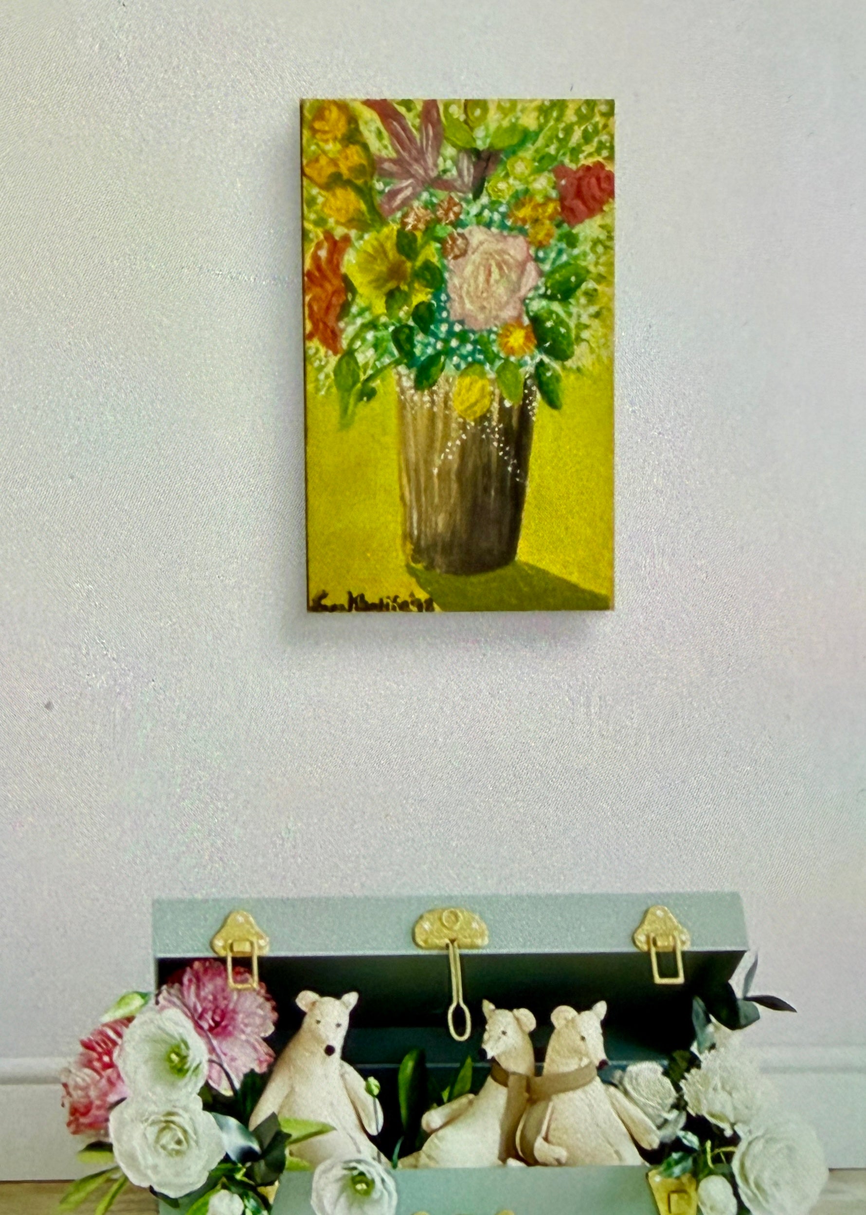 Floral painting on a wall above a decorative box with teddy bears and flowers.