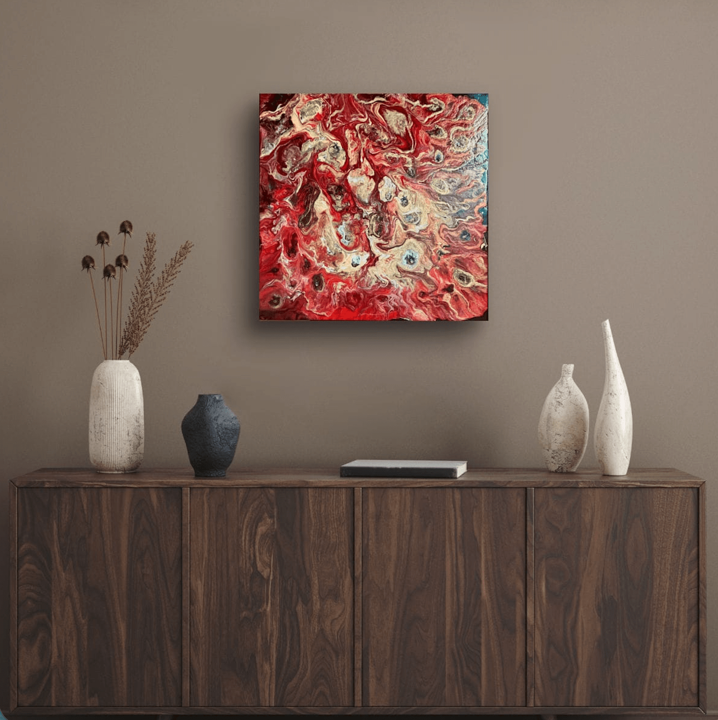 Abstract square wall art with swirling red, copper, and gold tones hanging above a dark wood console table with decorative vases.
