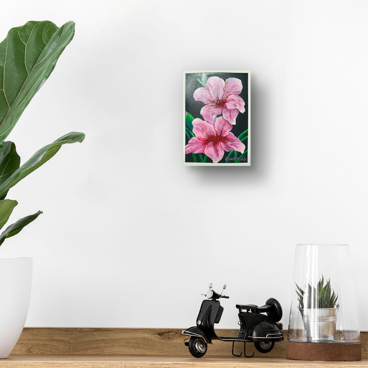 Framed floral artwork of an original acrylic painting of two pink blossoms on dark background, botanical floral art by Eman Khalifa, on a wall above a wooden shelf with decorative items.