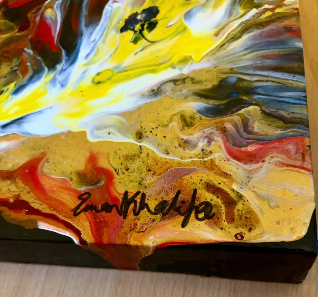Abstract art piece with swirling colors and a signature on a wooden surface